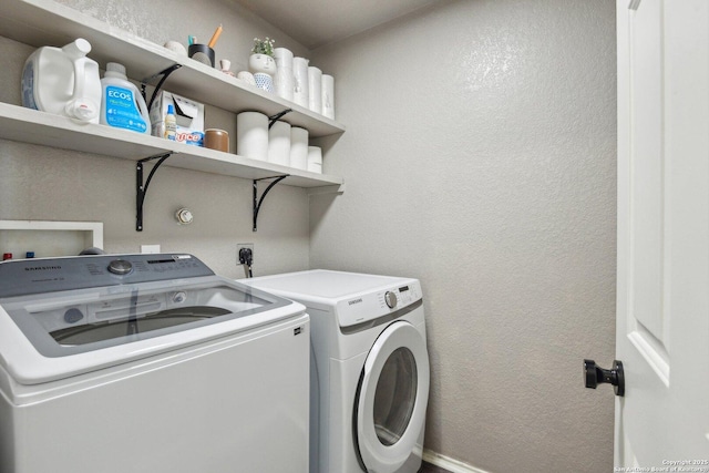 clothes washing area with a textured wall, laundry area, and separate washer and dryer