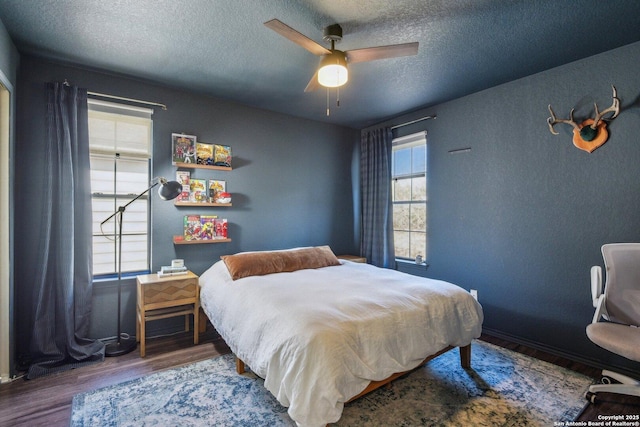 bedroom with a textured ceiling, a ceiling fan, wood finished floors, and a textured wall