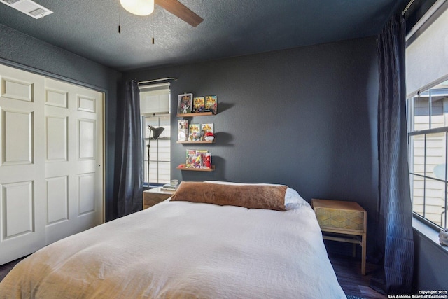 bedroom featuring a ceiling fan, visible vents, a textured ceiling, and wood finished floors