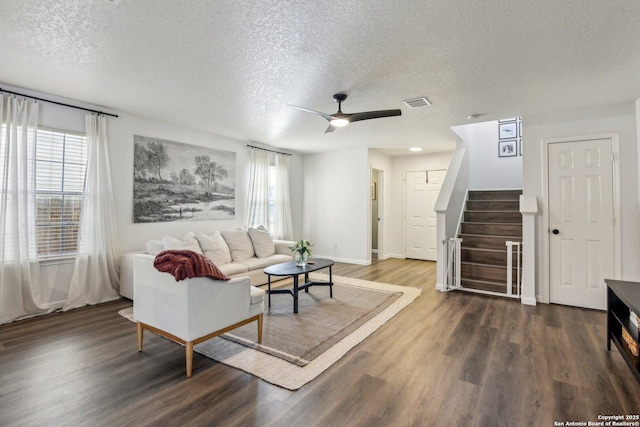 living room with a textured ceiling, wood finished floors, visible vents, a ceiling fan, and stairs