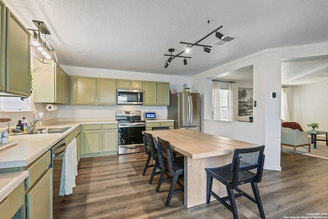 kitchen featuring green cabinets, appliances with stainless steel finishes, a sink, a textured ceiling, and a kitchen bar