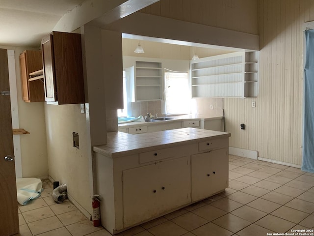 kitchen featuring tile countertops, wood walls, open shelves, and a sink