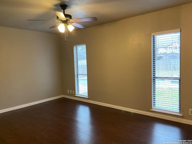 unfurnished room featuring dark wood-type flooring, a wealth of natural light, and baseboards