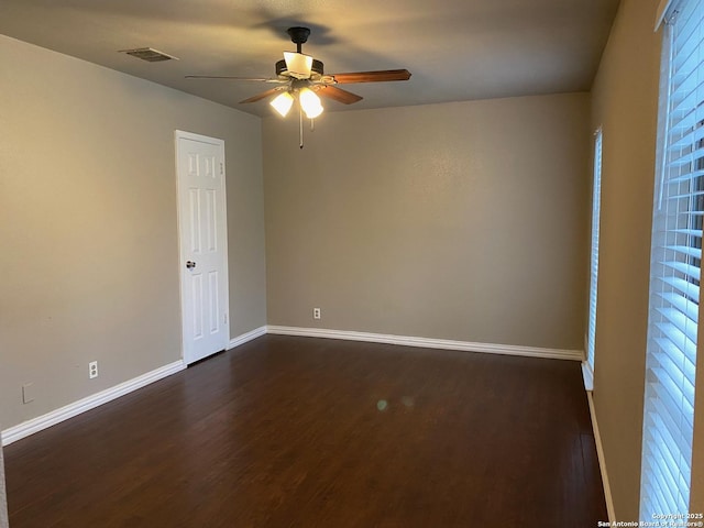 spare room with dark wood-style floors, visible vents, ceiling fan, and baseboards