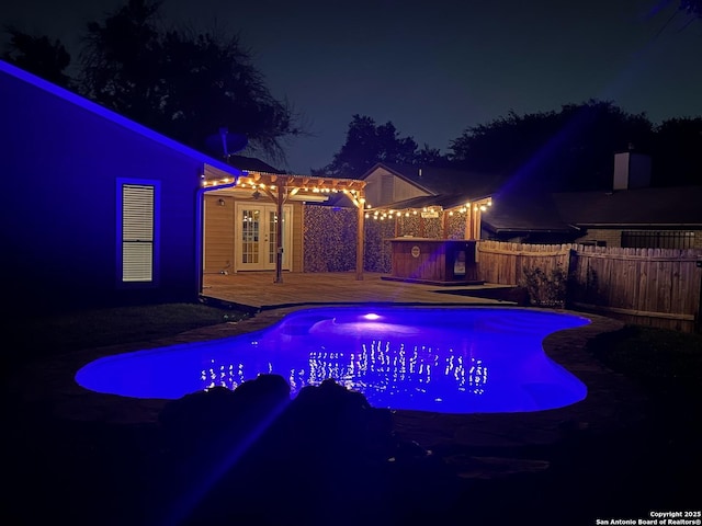 pool at twilight with fence, a deck, a pergola, and french doors