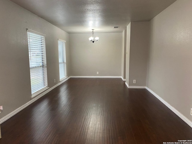 unfurnished room featuring dark wood-style floors, a notable chandelier, visible vents, a textured ceiling, and baseboards