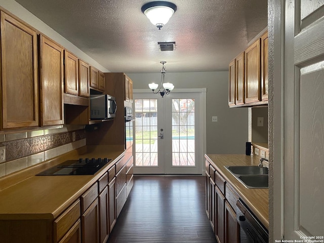 kitchen featuring visible vents, dark wood-style floors, black appliances, a chandelier, and a sink