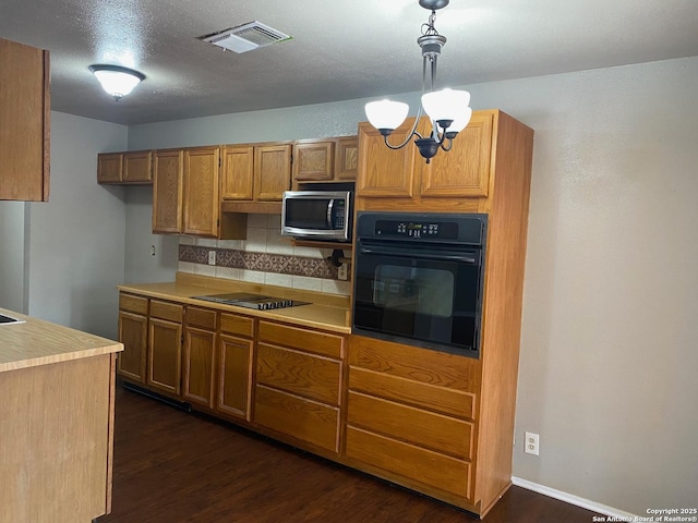 kitchen with brown cabinetry, light countertops, visible vents, and black appliances