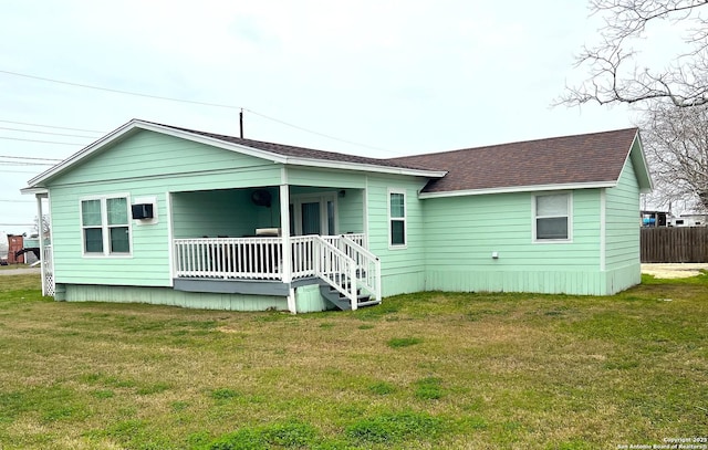 rear view of house featuring a shingled roof, a porch, and a yard