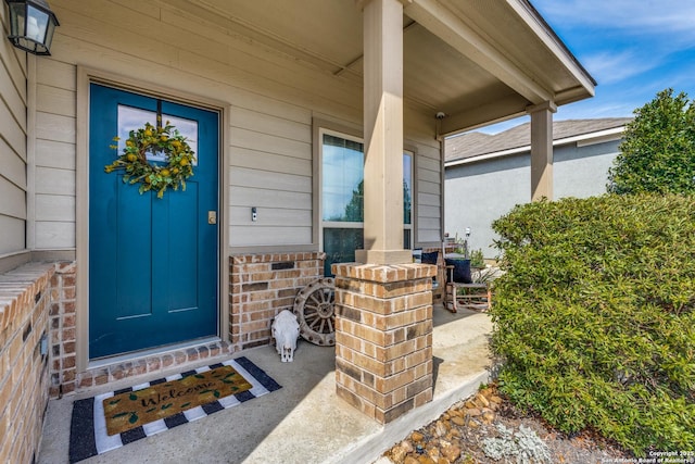 view of exterior entry featuring a porch and brick siding