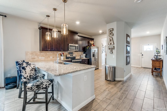 kitchen with dark brown cabinetry, tasteful backsplash, light stone counters, a breakfast bar, and stainless steel appliances