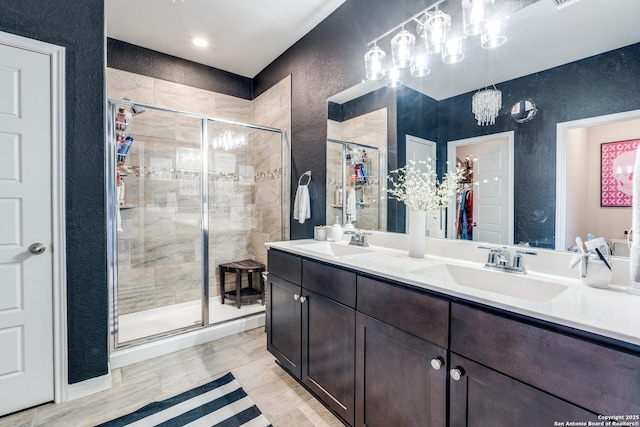 full bathroom with a textured wall, a stall shower, a sink, and double vanity