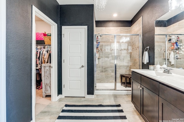 bathroom with a textured wall, a shower stall, vanity, and a walk in closet