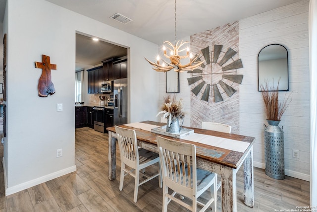 dining space featuring light wood finished floors, baseboards, visible vents, and a notable chandelier