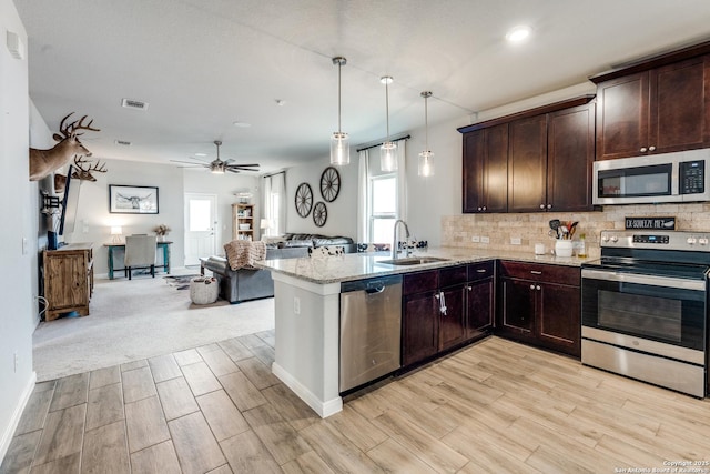 kitchen with dark brown cabinetry, a sink, visible vents, open floor plan, and appliances with stainless steel finishes