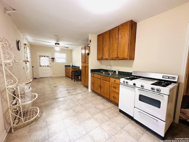 kitchen featuring brown cabinets, dark countertops, a ceiling fan, a sink, and white gas range oven