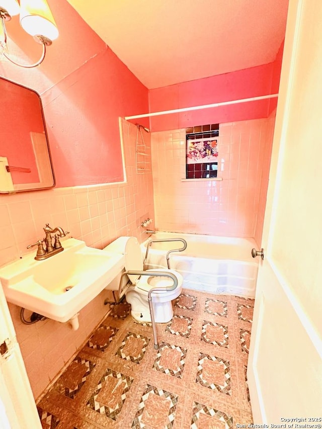 bathroom with toilet, a wainscoted wall, a sink, tile walls, and tub / shower combination