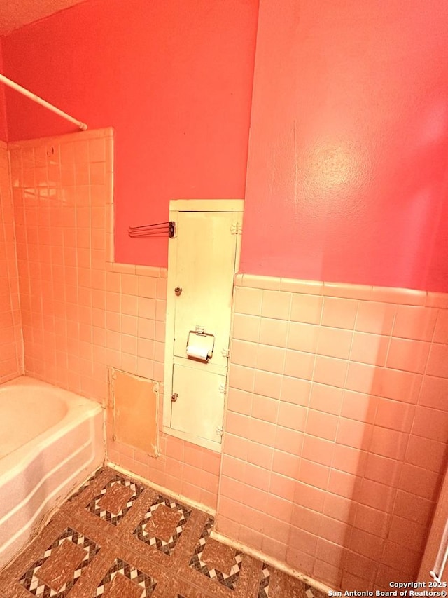 full bathroom with tile patterned floors, bathtub / shower combination, tile walls, and wainscoting