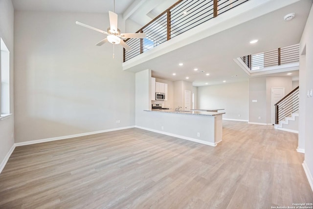 unfurnished living room featuring high vaulted ceiling, light wood-style flooring, a ceiling fan, baseboards, and stairs