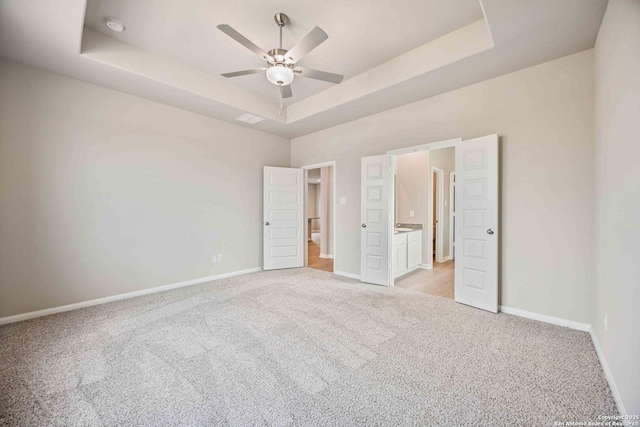 unfurnished bedroom with a tray ceiling, light colored carpet, baseboards, and ensuite bathroom