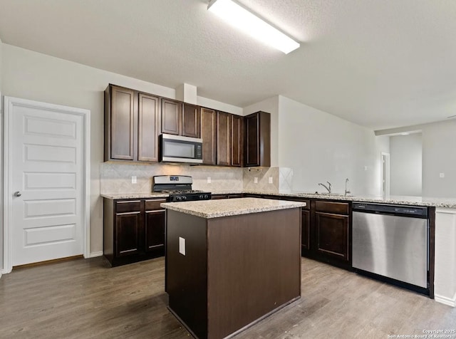 kitchen with dark brown cabinetry, decorative backsplash, appliances with stainless steel finishes, wood finished floors, and a sink