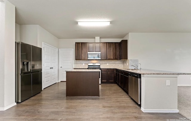 kitchen featuring dark brown cabinetry, wood finished floors, a sink, a kitchen island, and appliances with stainless steel finishes