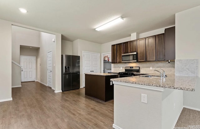 kitchen with dark brown cabinetry, decorative backsplash, a kitchen island, appliances with stainless steel finishes, and a sink