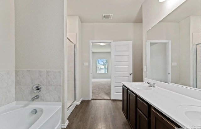 bathroom with double vanity, visible vents, wood finished floors, a sink, and a bath