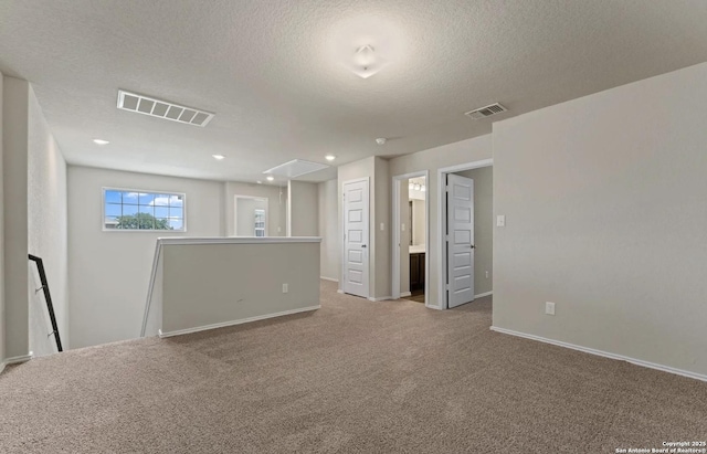 carpeted empty room featuring attic access, visible vents, a textured ceiling, and baseboards