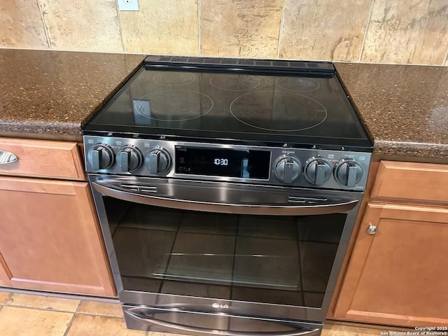 room details featuring stainless steel electric range oven, tasteful backsplash, dark stone countertops, and brown cabinets