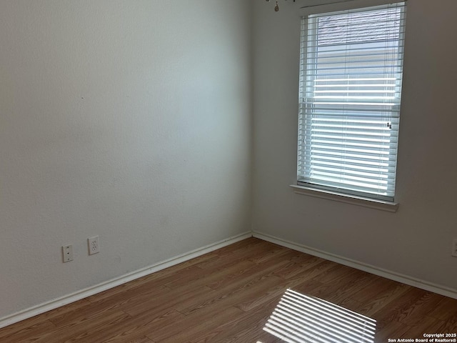 unfurnished room featuring plenty of natural light, baseboards, and wood finished floors