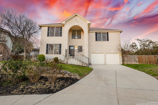 traditional-style home featuring brick siding, driveway, an attached garage, and fence