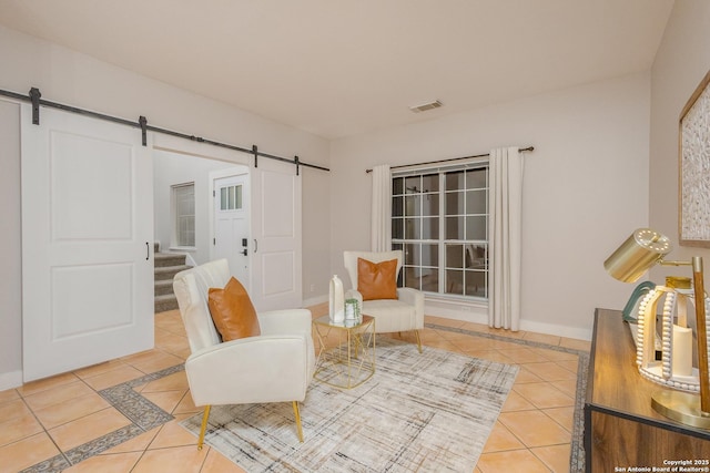 sitting room with a barn door, tile patterned flooring, visible vents, and baseboards