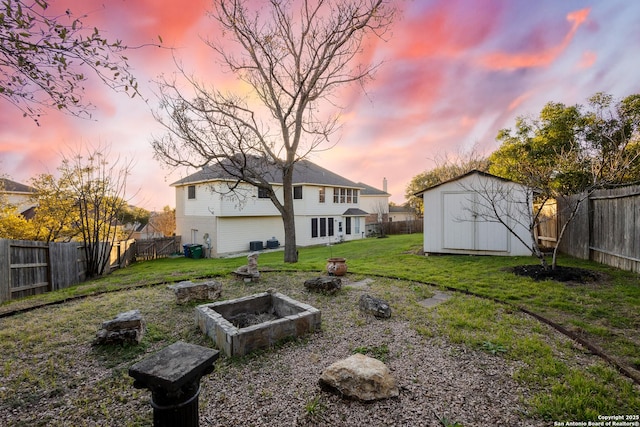 rear view of property with a fenced backyard, a fire pit, an outdoor structure, a yard, and a shed