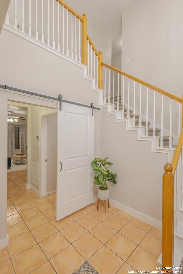 stairs featuring a barn door, baseboards, ceiling fan, tile patterned flooring, and a high ceiling