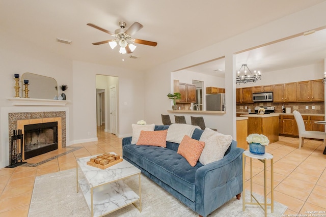 living area with light tile patterned floors, baseboards, visible vents, a fireplace, and ceiling fan with notable chandelier