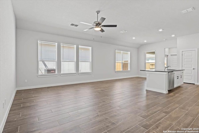 unfurnished living room featuring a sink, wood finished floors, baseboards, visible vents, and a ceiling fan