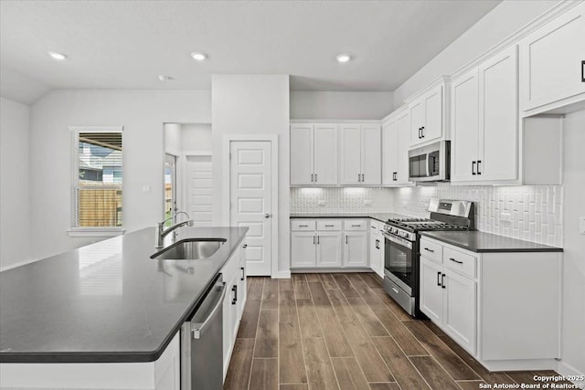 kitchen featuring wood finish floors, stainless steel appliances, dark countertops, white cabinetry, and a sink