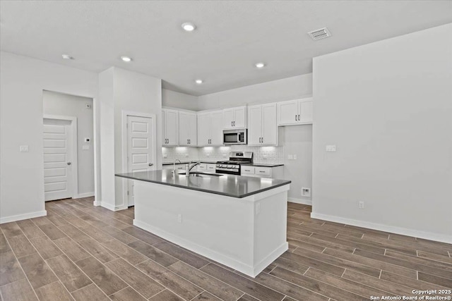 kitchen featuring visible vents, dark countertops, stainless steel appliances, wood finish floors, and a sink