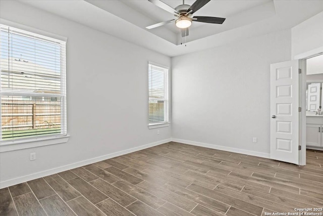 spare room featuring baseboards, a raised ceiling, a ceiling fan, and wood finish floors