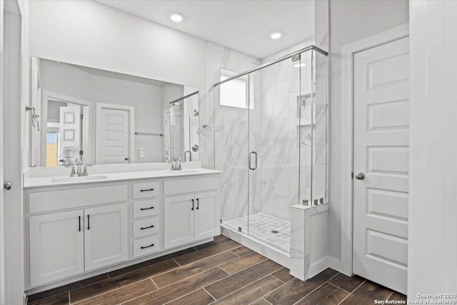 bathroom with double vanity, a sink, a marble finish shower, and wood tiled floor