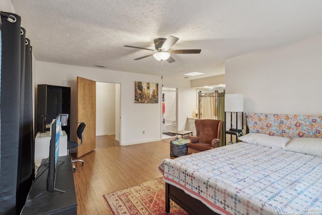 bedroom featuring visible vents, a ceiling fan, a textured ceiling, wood finished floors, and baseboards