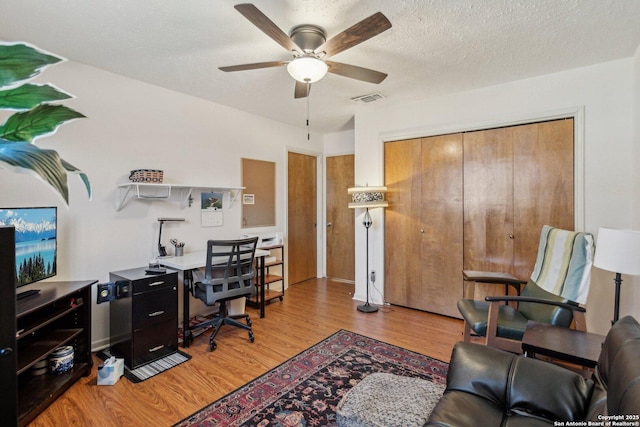 office space featuring light wood-style floors, visible vents, a textured ceiling, and a ceiling fan