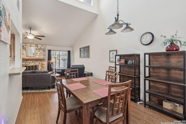 dining area with high vaulted ceiling, a ceiling fan, a fireplace, and wood finished floors