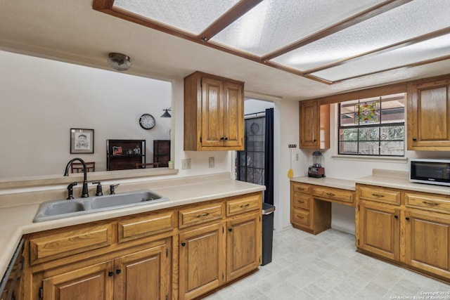 kitchen featuring stainless steel microwave, a sink, light countertops, light floors, and brown cabinetry