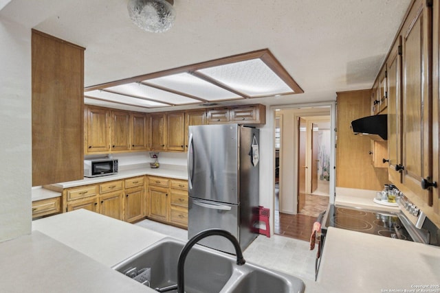 kitchen featuring brown cabinetry, appliances with stainless steel finishes, range hood, light countertops, and a sink