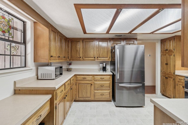 kitchen featuring brown cabinetry, light countertops, and freestanding refrigerator