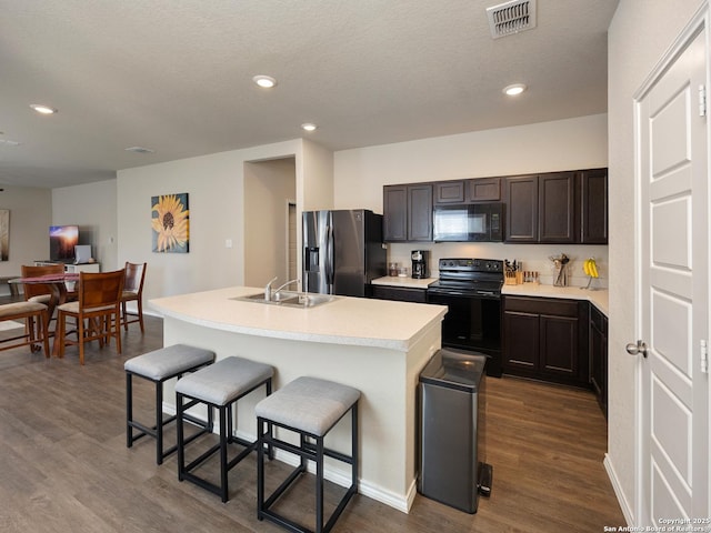 kitchen featuring a sink, visible vents, a kitchen breakfast bar, light countertops, and black appliances