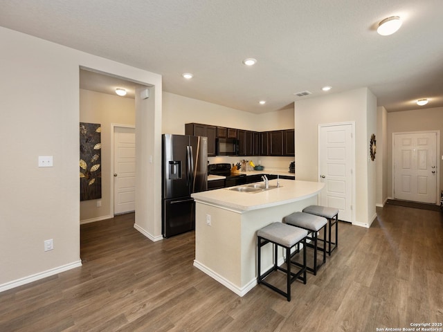 kitchen with light countertops, dark wood-type flooring, black appliances, an island with sink, and a kitchen bar