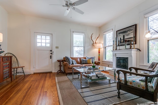 living area featuring light wood-type flooring, baseboards, a ceiling fan, and a glass covered fireplace